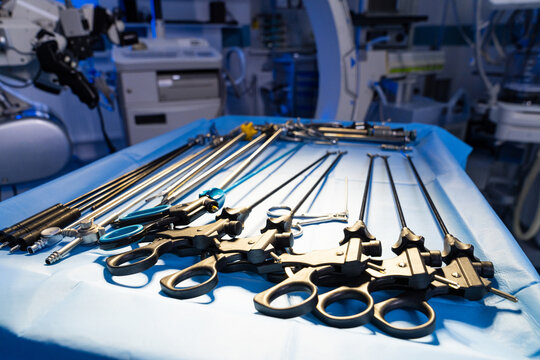 Laparoscopic surgical graspers and trocars on sterile blue drape. Row of long shaft laparoscopic instruments and trocars in an operating room with medical equipment.