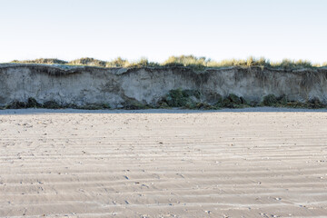 Flat sandy beach by an eroding cliff and marram grass sand dunes