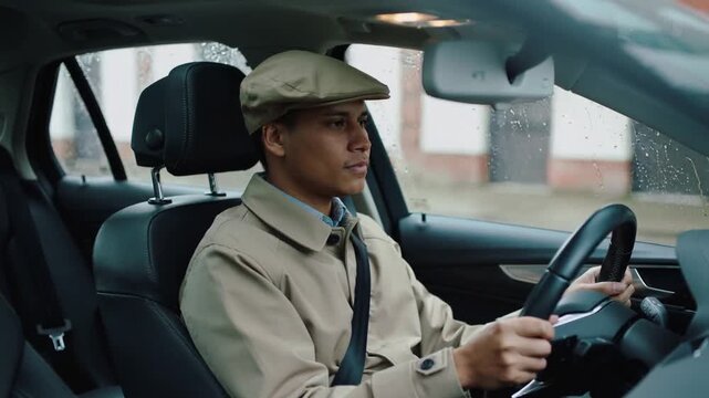 Driving man in beige trench coat in sedan during light rain, holding wheel with seatbelt