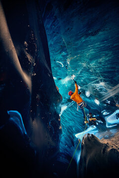 Man climbing frozen ice cave in winter mountains