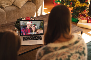 Naklejka premium Mother and daughter making christmas laptop video call with smiling caucasian couple in santa hats