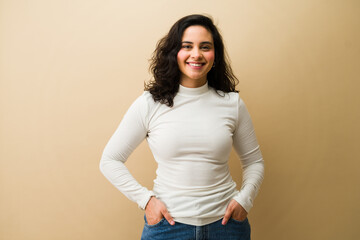 Happy young woman smiling, feeling confident and successful, standing against a beige background,...