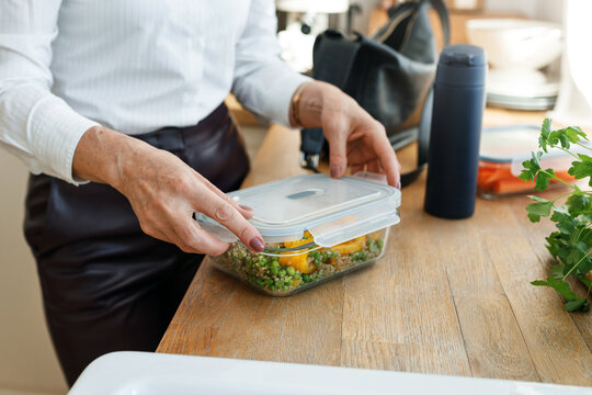 Closeup of unrecognizable female hands of senior office worker or real estate agent in formal wear packing healthy snack to have lunch at work, without spending extra time and focus on project