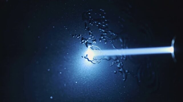 Emitting blue beam from right emitter striking wet film in lab, forming ripples, spraying droplets