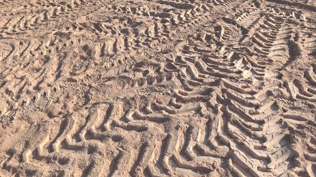 View of intricate tire patterns imprinted on soft earth. The golden-yellow soil creates a textured landscape of dusty trails left by passing vehicles.