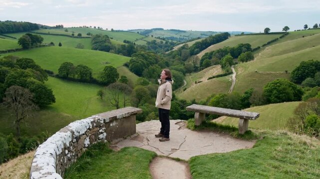 Arriving hiker pausing, surveying valley from stone overlook with beige anorak and boots