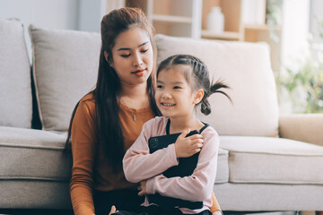 Obraz premium A cheerful Asian mother helps her young daughter do homework and color a book at home, while the father works on a laptop in the background. A cozy, bright, and modern family lifestyle.