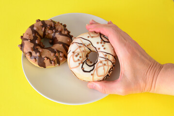 Hand holding a delicious glazed donut with another on a plate flat lay