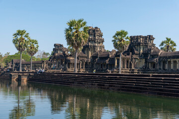 Angkor Wat, Cambodia, the temple, seen through across the lake trees with many tourists.