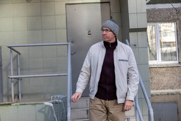 Man in a knit hat and jacket standing near a building entrance. Urban street scene with everyday life