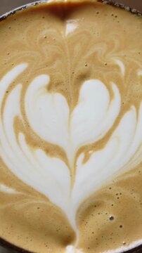 Vertical video: Showing cooling, cup of latte settling on tabletop, milk rosetta pattern holding