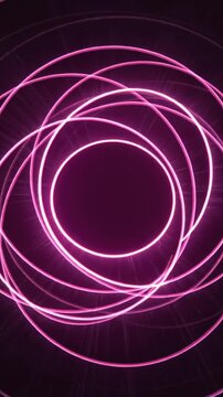 Vertical video: Rotating neon pink light trails forming spirals in studio, triggered by LED for art