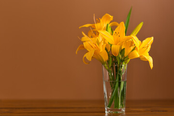 Glass vase filled with blooming orange daylilies on a brown background