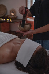 Therapist holding singing bowl near client on massage table Vertical