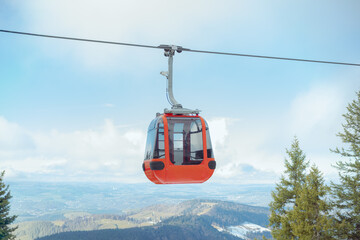 A red panoramic cable car gondola suspended high above an alpine valley with rolling hills and distant villages under a cloudy blue sky © Pablo