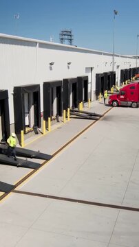 Vertical video: Passing white trailer, worker in hi-vis vest running across apron toward dock ramps