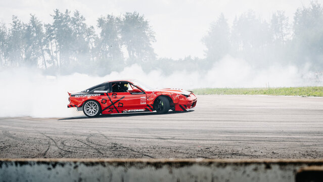 Nissan S13 200SX drifting on asphalt track. Dynamic, side-profile shot of a modified red sports car mid-drift in a massive cloud of thick white tire smoke. Chaiky, Ukraine - August 02 2025