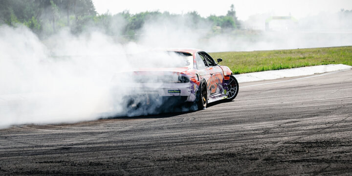 orange Nissan Silvia S14 drift car exiting a turn with smoke. Dynamic rear-angle shot of a modified  sportscar as it slides through a corner on an asphalt track. Chaiky, Ukraine - August 02 2025