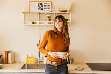 Woman smiling holding coffee cup in modern kitchen