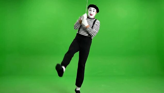 A mime swinging on an invisible trapeze bar in mid-air against a vibrant green background from a dynamic front viewpoint