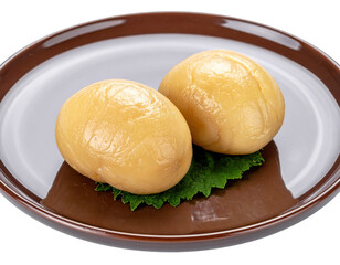 Two glistening yellow dumplings resting on a single green leaf on brown plate