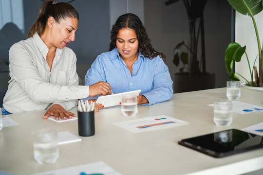 Business women sharing ideas inside company office - Females latin colleagues discussing new financial project - Brainstorming, entrepreneur and corporate concept - Main focus on right girl face