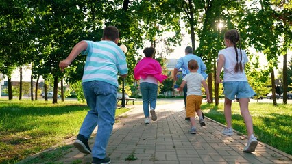Obraz premium Family playing in city park. Parents, kids boys play running in city park summer. Dad mom, sons children having fun run city street. Concept parenting. Happy family. Happy people dad mom son, daughter