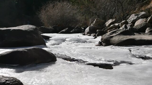 4K partially frozen mountain creek with flowing water under ice in winter, Colorado