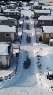 Vertical video: Gliding drone revealing row of trailers in snowy park with cleared path and truck