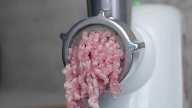 Close-up of an electric meat grinder processing raw meat into fresh minced meat. Domestic kitchen appliance grinding meat through a metal nozzle for cooking