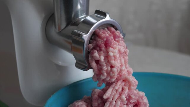 Close-up of an electric meat grinder mincing raw meat into fresh stuffing in a bowl. Professional kitchen appliance processing meat for homemade meal preparation