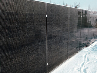 Modern solar panel array installed as a fence in a snowy backyard during winter.