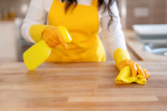 Person cleans a wooden surface with spray and cloth in a kitchen setting during daytime