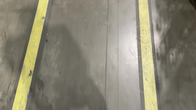 Point of view walking on a grey industrial concrete floor between two parallel yellow safety lines