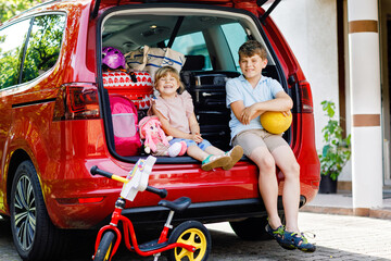 Two children, school boy and preschool girl sitting in car trunk before leaving for summer vacation with parents. Happy kids, siblings, brother and sister with suitcases and toys going on journey © Irina Schmidt