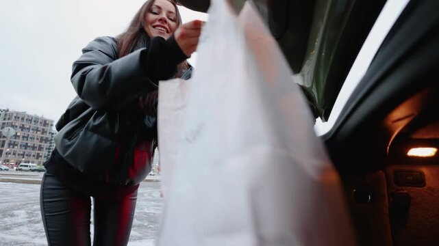 A low-angle, Dutch-tilt video from trunk level. A stylish young woman stands by her car as the trunk opens automatically to load groceries and shopping bags.