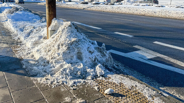 Dirty snow pile along city road during winter. Plowed snow mixed with sand and road salt in urban environment.
