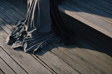 The textures of a dark draped fabric interact with the light and shadows on a rustic wooden surface, creating a striking contrast and a sense of depth and comfort.