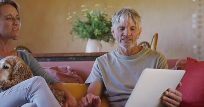 Senior caucasian couple using tablet and sitting with dog in living room