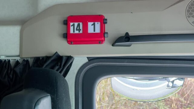 View from inside a truck cab showing a red height indicator sign above a window with a convex safety mirror