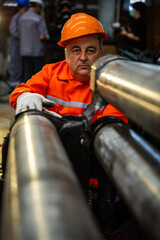 Serious industrial worker wearing orange protective safety gear and helmet meticulously inspecting...