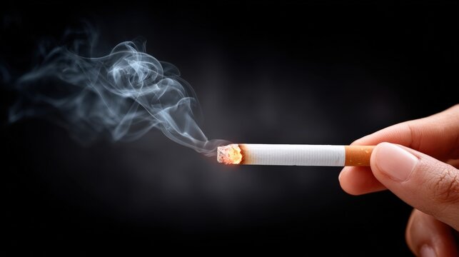 Hand holding a lit cigarette with smoke curling upwards against a dark background, showcasing the glowing tip and the textured paper of the cigarette in sharp focus