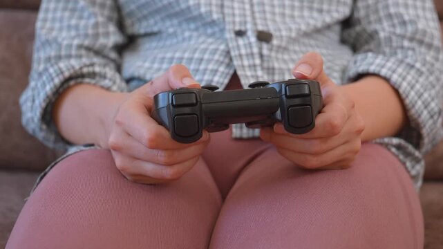 Unrecognizable woman holding a joystick and playing video games on a console at home, pressing the buttons on the controller and having fun during her leisure time on the couch