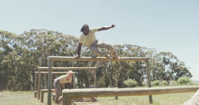 Diverse group of soldiers going over and under hurdles on army style obstacle course in the sun