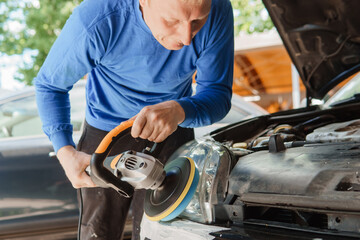 Obraz premium Man polishing car headlight with a power buffer. Automobile detailing and car care service concept for vehicle maintenance and repair.