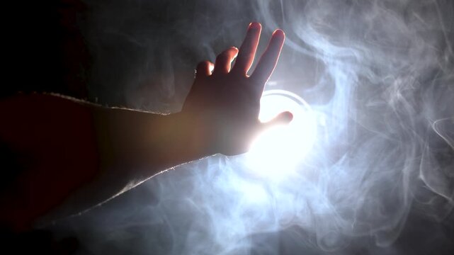 A man's hand reaches for the light, a video concept. To reach for the light, to strive for the truth, the light of a powerful spotlight hits the frame, volumetric lighting, the rays shine through the 