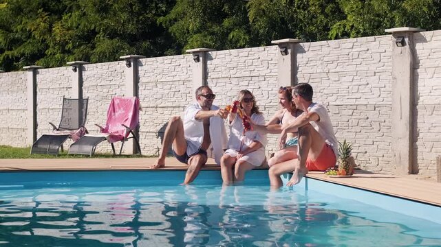 Group of adult friends sitting and relaxing next to outdoor pool.