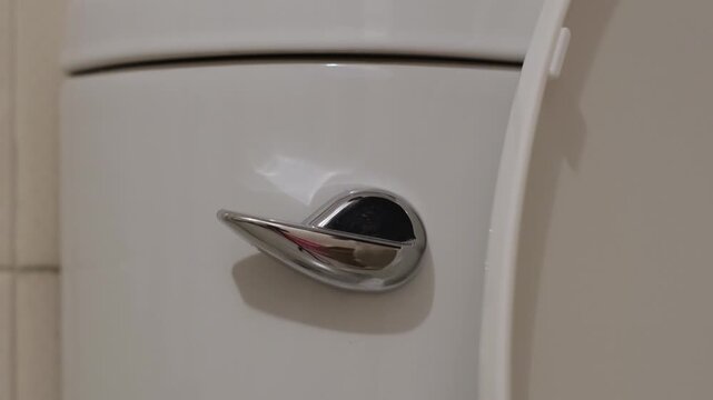 Finger pressing a toilet flush lever creating a mechanical clunk and rushing water sound