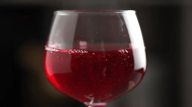 Close-Up Slow Motion of Red Wine Being Poured into a Glass, Creating Bubbles and Dynamic Movement Against a Dark Background.