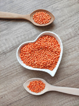 Dried small red lentils in a decorative plate and wooden spoons on a wooden background